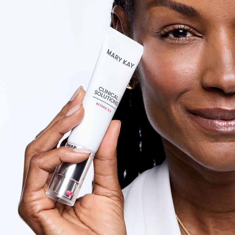 Dark-skinned woman holding Mary Kay Clinical Solutions Retinol 0.5 tube against a light background.